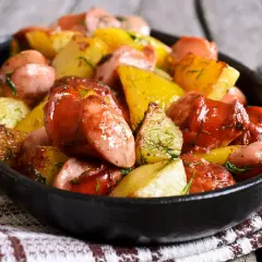 Pyszne dania z ziemniaków i kiełbasy, okraszone koperkiem, podane w czarnej patelni.
