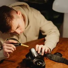 A young person carefully performs camera cleaning, using a blower to remove dust from their DSLR.