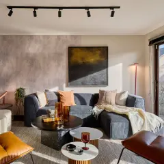 Sofá gris, mesas de centro, sillones de cuero y detalles decorativos. Los **colores que dan luz y amplitud** crean un ambiente acogedor y moderno.