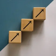 Trzy drewniane kostki tworzą schody, każda z czarną strzałką w górę. To symboliczne ten square games akcje, które rosną.