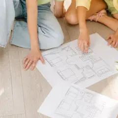 Dwie osoby analizują plany domu, przygotowując się do uzyskania pozwolenia na budowę.