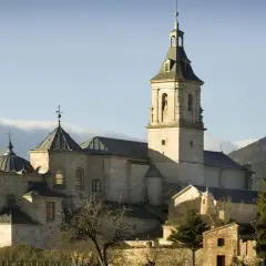 El imponente monasterio del Paular se alza bajo un cielo azul, con sus cúpulas y campanario de piedra bañados por el sol.