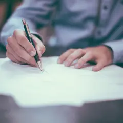 Dłoń pisząca długopisem na papierze.