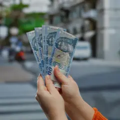 Ręce trzymające banknoty 1000 forintów. W tle widać ulicę, co sugeruje, że chodzi o ceny na Węgrzech.