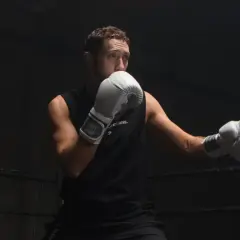 Boxer in white gloves practices a boxing slip in a dark ring, ready for the next round.
