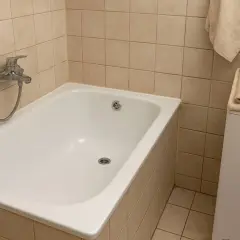 Biała wanna w łazience z beżowymi płytkami. Czy renowacja wanny to dobry pomysł? Obok pralka z ręcznikami.