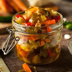 Un frasco de vidrio lleno de escabeche de verduras, con trozos de pimientos y zanahorias.