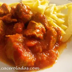 Sabroso carne de cerdo con tomate de la abuela, jugoso y tierno, acompañado de patatas fritas crujientes.