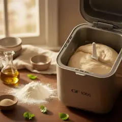 Machine à pain avec une belle pâte levée prête à cuire. Farine, levure et huile à proximité.