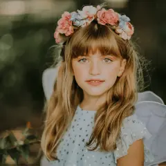 Urocza dziewczynka w kwiecistym wianku i skrzydłach, nosząca piękne ozdoby do włosów dla dzieci.