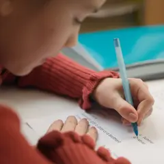 Dziecko w czerwonym swetrze pisze długopisem po kartce. Czy to zadanie z języka angielskiego, od jakiej średniej jest 5?