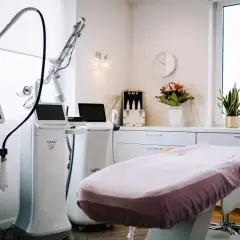 Gabinet zabiegowy z nowoczesnym sprzętem, w tym laser frakcyjny. Czyste, jasne wnętrze z łóżkiem zabiegowym i dekoracjami.