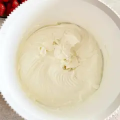 Gładki, puszysty krem z mascarpone w białej misie, gotowy do deseru. Obok miski widać truskawki.