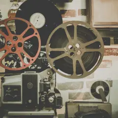 Stary projektor filmowy, taśmy filmowe i płyta winylowa na tle ceglanej ściany.