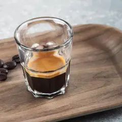 En liten shot med espresso, med crema, bredvid kaffebönor på en träbricka. En perfekt start på dagen, en stark espresso vs. vanligt kaffe.