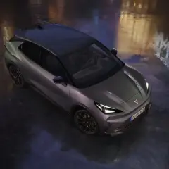 Nowoczesny Cupra Raval w ciemnoszarym kolorze, z czarnym dachem, stoi na mokrej nawierzchni, odbijając światła miasta.