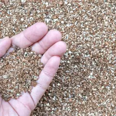 Main d'une personne tenant une poignée de vermiculite, un matériau léger et poreux. Sa composition est idéale pour l'horticulture.