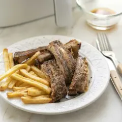 Costillas jugosas y patatas fritas crujientes, recién salidas de la freidora de aire. Un plato perfecto para disfrutar.