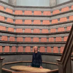 En kvinna står i den imponerande **anatomiska teatern Uppsala**. De rödbruna väggarna med sina pelare skapar en unik atmosfär.