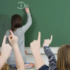 Lehrerin schreibt "De" an Tafel, Schüler heben Hände. Einblick in die bildungspolitik deutschland.
