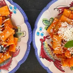 Deux assiettes de rigatoni alla norma, garnies de basilic frais et de fromage râpé, sur des plats décorés de poissons colorés.