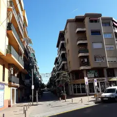 Calle soleada en Les Roquetes del Garraf, con edificios residenciales y comercios.