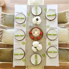 Tavola apparecchiata per una festa a tema chic, con sedie in bambù bianco e cuscini decorati.