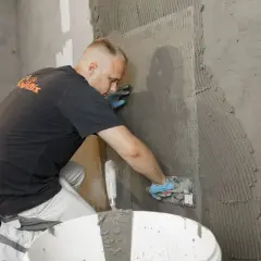 Mann trägt Mörtel auf ein Armierungsgewebe auf, um die Kellerwand von innen abzudichten.