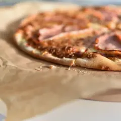 Zbliżenie na pizzę z szynką na papierze do pieczenia.