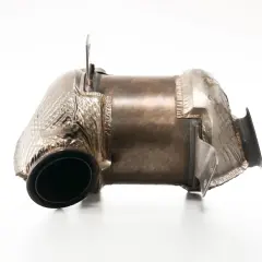 Metalowy element układu wydechowego, przypominający kształtem tłumik lub fap, z widocznymi zgrubieniami i mocowaniami.