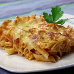 Porción de macarrones al horno gratinados con queso derretido y una hoja de perejil, servida en un plato blanco.