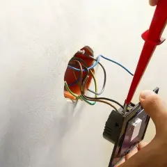 Instalator podłącza podwójny włącznik światła, używając próbnika do przewodów. Pokazano, jak podłączyć włącznik światła podwójny trzy przewody.