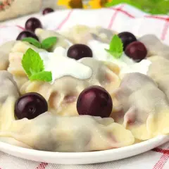 Pyszne pierogi z wiśniami, polane śmietaną i ozdobione świeżymi wiśniami i miętą. Letnia uczta na talerzu.