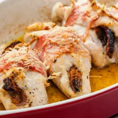 Pyszne roladki z kurczaka zawinięte w boczek, zapieczone z suszonymi pomidorami i posypane parmezanem, w sosie własnym.