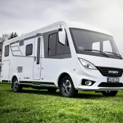 Biała kamper z serii Hymermobil, produkt Erwin Hymer Group, stoi na zielonej trawie.