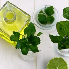 Aceite amarillo en botella, menta y lima, ingredientes para un enjuague bucal para llagas casero.
