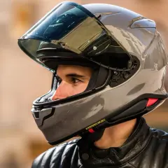 Hombre con casco moto 125 gris brillante, visor oscuro y chaqueta de cuero negra.