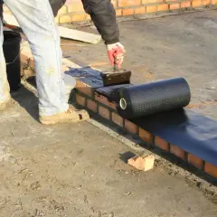 Pracownik nakłada abizol na ceglaną ścianę, przygotowując ją do dalszych prac budowlanych.
