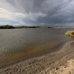 Aguas tranquilas en la rambla Morales bajo un cielo nublado. Arena y vegetación bordean la orilla.