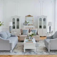 Salotto in stile shabby con divani grigi, poltrone, tavolino bianco, specchio dorato e vetrine.