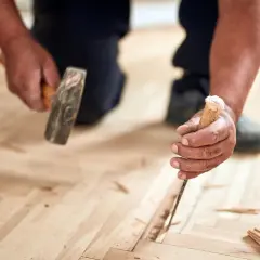 Un artisan utilise un ciseau et un marteau pour changer une lame de parquet flottant endommagée.