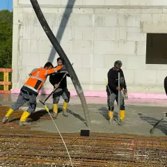Arbeiter gießen Beton für die Bodenplatte. Sie schalen die Platte aus und verteilen den frischen Beton mit Werkzeugen.