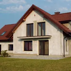 Dom w budowie z brązowym dachem, w tle linia wysokiego napięcia.