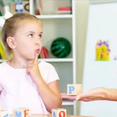 Dziewczynka z palcem przy ustach myśli podczas zabawy edukacyjnej z literkami.
