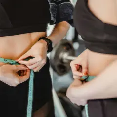 Donna in palestra misura la vita con un metro, segno di un percorso di dimagrimento.