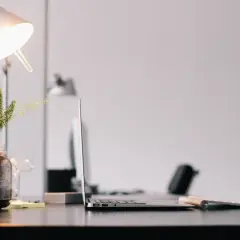 Escritorio con portátil, teclado y un flexo moderno iluminando una planta en un frasco.