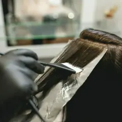 Fryzjer nakłada farbę na włosy za pomocą pędzla i folii.