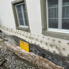 Arbeiten am Haus: Das Fundament trockenlegen mit neuer Abdichtung und Drainage. Gerüst und Baumaterialien sind sichtbar.
