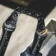 Gloved hands clean a RockShox Revelation RC fork, removing dirt from the stanchions.