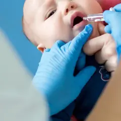 Ein Baby erhält Tropfen zur Vorbeugung von Rotavirus-Symptomen. Blaue Handschuhe schützen die Hände des Arztes.